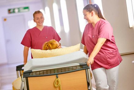 zwei Auszubildende der Pflege schieben ein Patientenbett